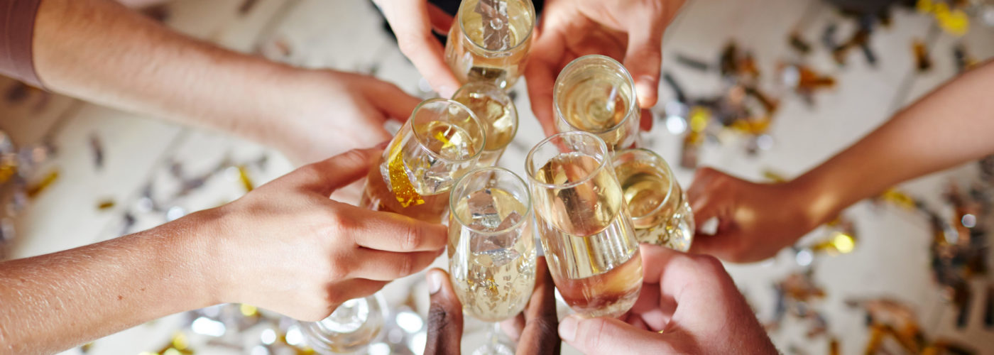 Several flutes with sparkling champagne in hands of intercultural friends during toast